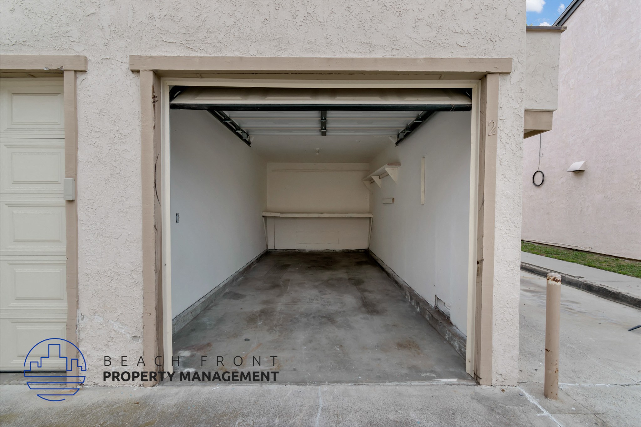 A white garage door is open to reveal a concrete floor.